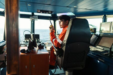 Filipino deck Officer on bridge of vessel or ship. He is speaking on GMDSS VHF radio