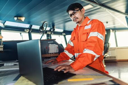 Filipino deck Officer on bridge of vessel or ship. He is using laptop, electronic paperwork at seaの写真素材