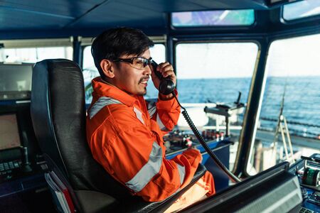 Filipino deck Officer on bridge of vessel or ship. He is speaking on GMDSS VHF radioの写真素材