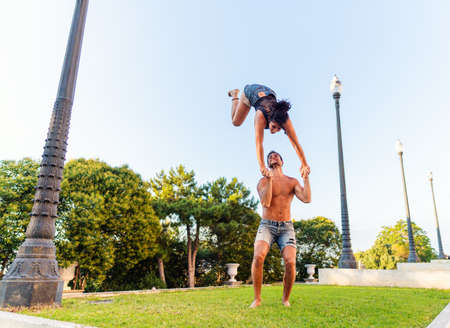 Beautiful man and woman doing acroyoga in the city park lawn