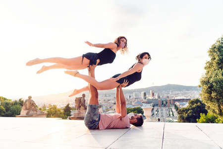 Beautiful man and two women doing acroyoga in the cityの写真素材