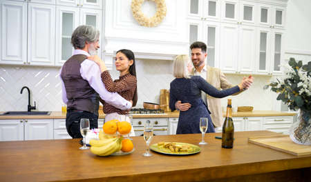 Two multigenerational couples dancing in kitchen when celebrating birthday