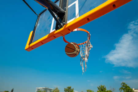 Basketball ball falling through old net. Blue sky on backgroundの写真素材