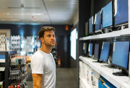 Pensive man choosing computer in storeの写真素材