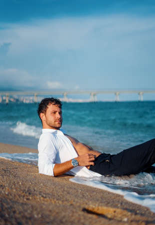 Masculine man relaxing on wet beach in eveningの写真素材