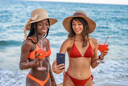 Girlfriends with cocktails and smartphone on beachの写真素材