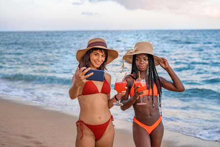 Happy girlfriends with cocktails taking selfie near seaの写真素材