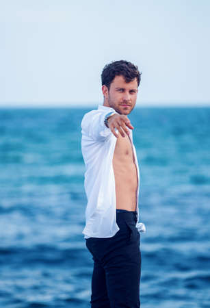 Stylish man reaching out hand on seashoreの写真素材