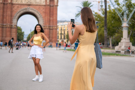 Woman taking photo of girlfriend in cityの写真素材