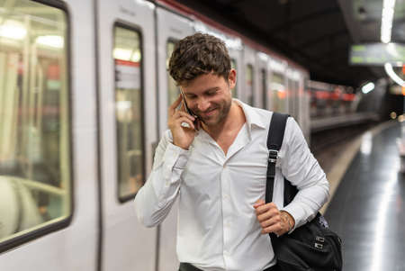 Glad businessman having smartphone conversation on stationの写真素材