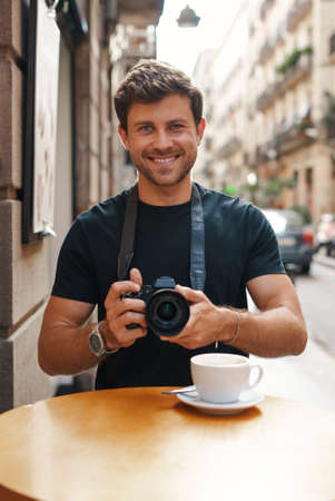 Smiling guy taking pictures on photo camera in street cafeの写真素材