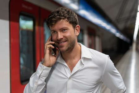 Positive male entrepreneur talking on smartphone near trainの写真素材