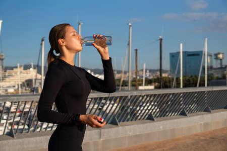 Sportswoman drinking water on embankmentの写真素材