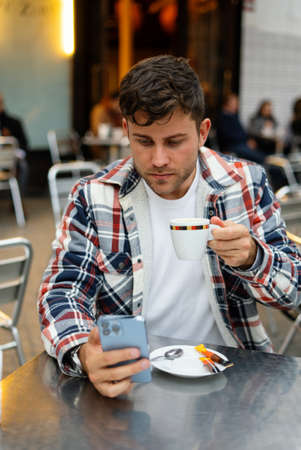 Man drinking coffee and browsing smartphone in street cafeの写真素材
