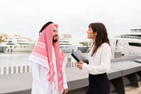 Two multiracial business partners standing in port and talking pleasantly after closing dealの写真素材