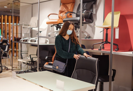 Young woman in white face protective mask choosing office furniture during covid-19 pandemicの写真素材
