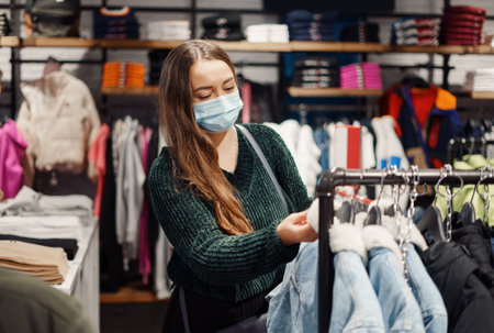 Photo of young mother in face mask walks around mall doing shoppingの写真素材