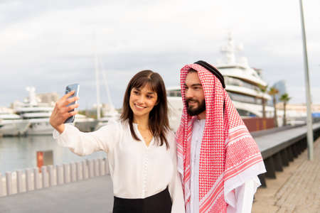 Smiling Arab businessman taking selfie on smartphone with young attractive female assistant in portの写真素材