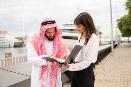 Satisfied arab man client signing contract at meeting with female business partner in portの写真素材