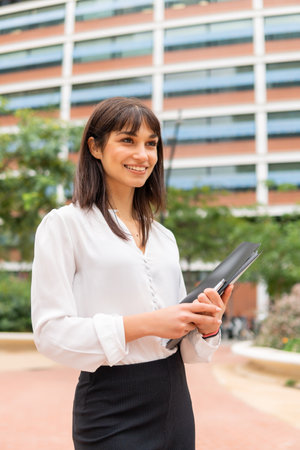 Attractive european businesswoman holding clipboard with documents while standing on city streetの写真素材