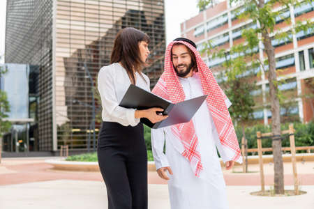 Young european female assistant showing contract document to arab businessman on city streetの写真素材