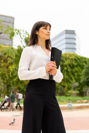 Outdoor photo of young confident european businesswoman in formal outfit with clipboardの写真素材