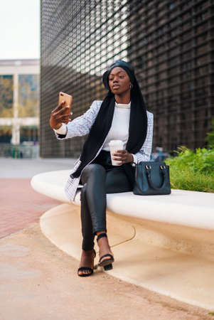 Positive stylish Muslim black woman taking selfie on smartphone