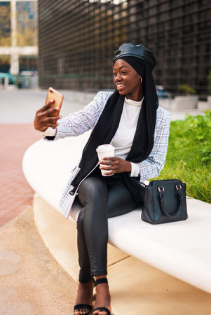 Positive stylish Muslim black woman taking selfie on smartphoneの写真素材