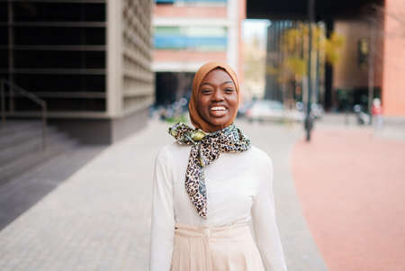 Smiling Muslim black woman in hijab standing near office buildingの写真素材