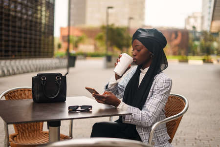 Black elegant woman drinking coffee and browsing smartphoneの写真素材