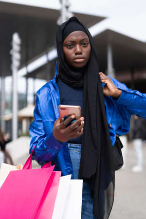 Muslim shopper with smartphone walking on streetの写真素材