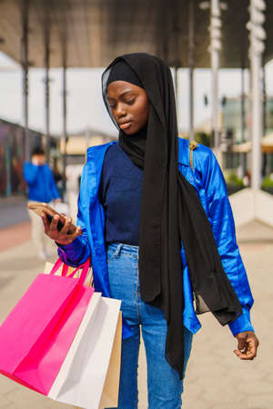Trendy Muslim woman browsing smartphone during shoppingの写真素材