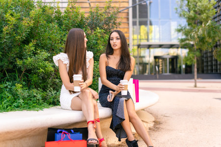 Stylish women with coffee chilling on bench after shoppingの写真素材