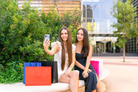 Fashionable girlfriends taking selfie on bench after shopping in boutiquesの写真素材