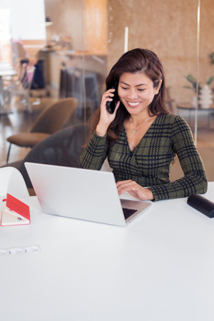 Happy lady receiving phone call while using netbookの写真素材