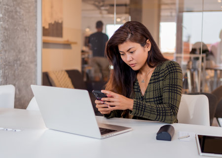 Focused woman using smartphone while working in officeの写真素材