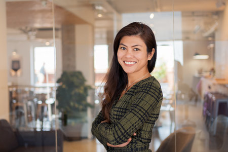 Smiling Asian worker with arms crossed in officeの写真素材