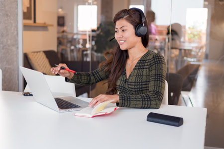Smiling lady in headset speaking online in officeの写真素材