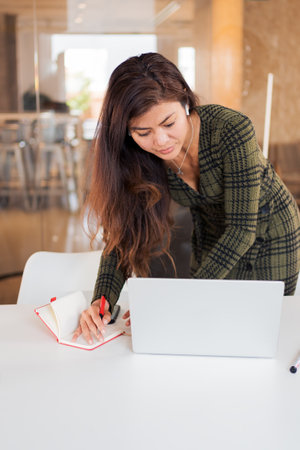 Busy woman taking notes while using laptopの写真素材