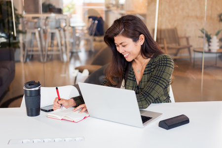 Cheerful female writing notes while working in officeの写真素材