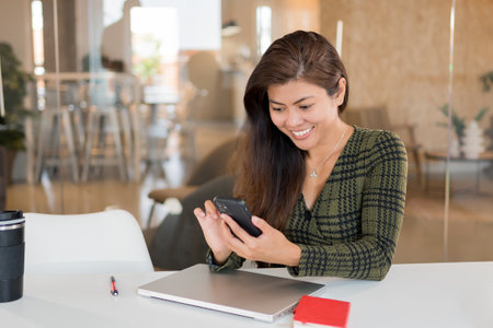 Cheerful woman using smartphone in office spaceの写真素材
