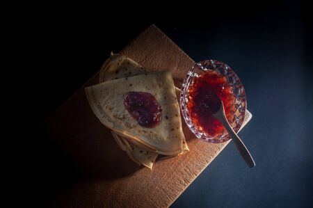Top view of homemade thin pancakes with strawberry jam leaves on a wooden table. Tasty sweet food....