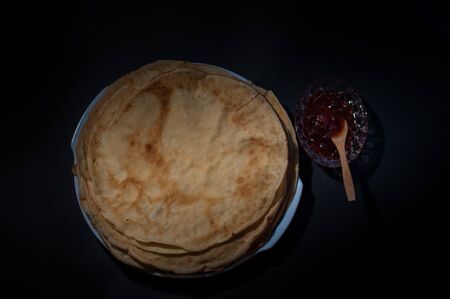 Top view of stack homemade thin pancakes with strawberry jam leaves on a plate. Tasty sweet food. Russian pancakes with strawberry and wooden spoon in front of dark backgroundの写真素材