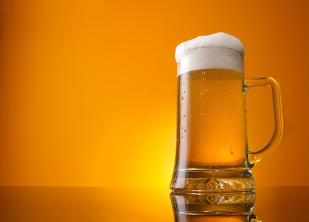 Glass of beer close-up with froth over orange backgroundの写真素材