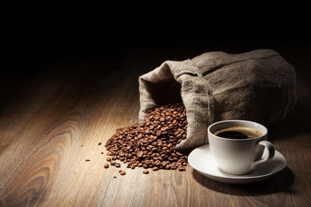 Coffee cup with burlap sack of roasted beans on rustic tableの写真素材