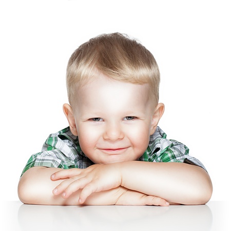 Portrait of a cute little boy smiling while sitting at table, isolated over whiteの写真素材