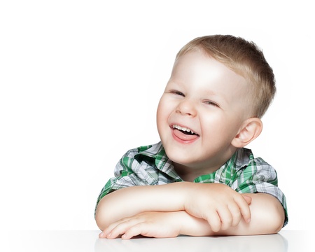 Portrait of a cute little boy smiling while sitting at table, isolated over whiteの写真素材