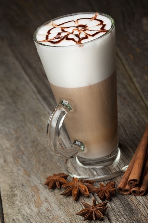 coffee cup and beans, cinnamon sticks, nuts and chocolate on wooden table on brown backgroundの写真素材
