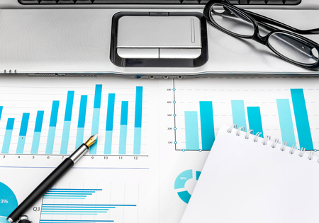Financial graphs with laptop, eyeglasses, pen and notepad on the workplace.の写真素材