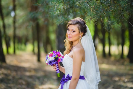 The girl in a wedding dress with a purple bow and a bouquet in the parkの写真素材